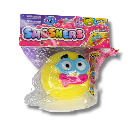 A packaged yellow squishy toy with a blue eyeglass face and pink tongue, sealed in clear plastic with a colorful 'Smushers' branded retail header card.