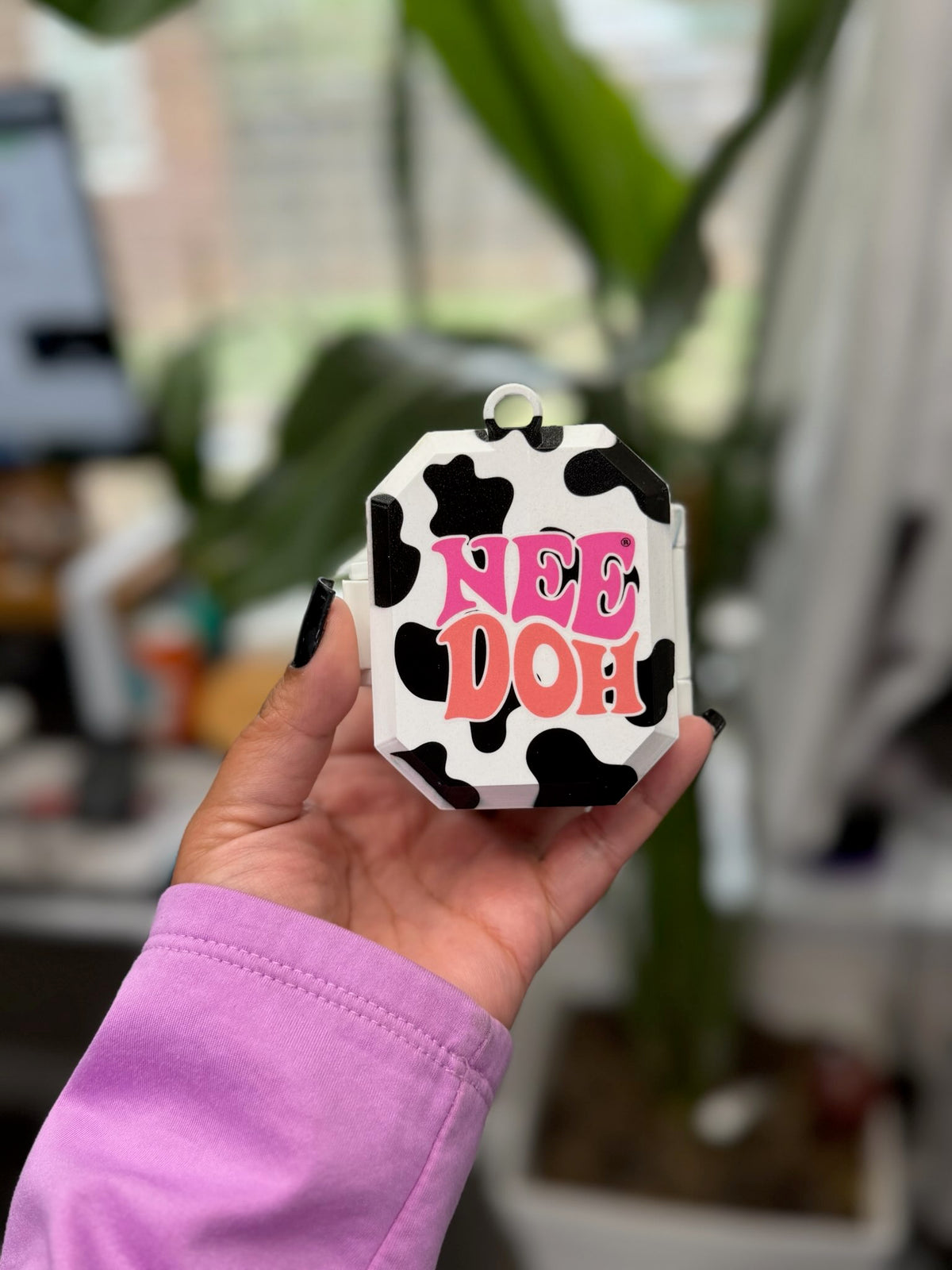 Front of cow print case showing NeeDoh lettering, side hinge, and hanging loop